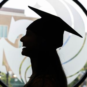Silhouette of a graduate wearing a cap in front of a UCF emblem in the background.