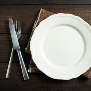 A white plate with a fork and knife placed on a napkin, set on a wooden table.