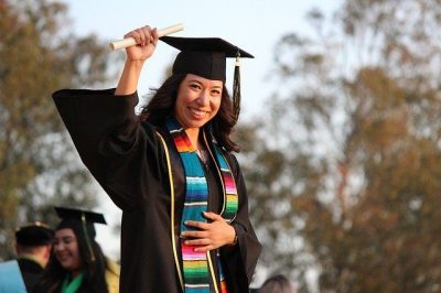 a student in graduation attire proudly holding their diploma to the sky