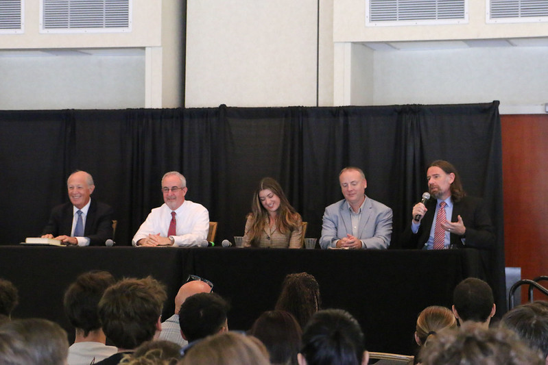 Five people sitting on a stage one with a mic.