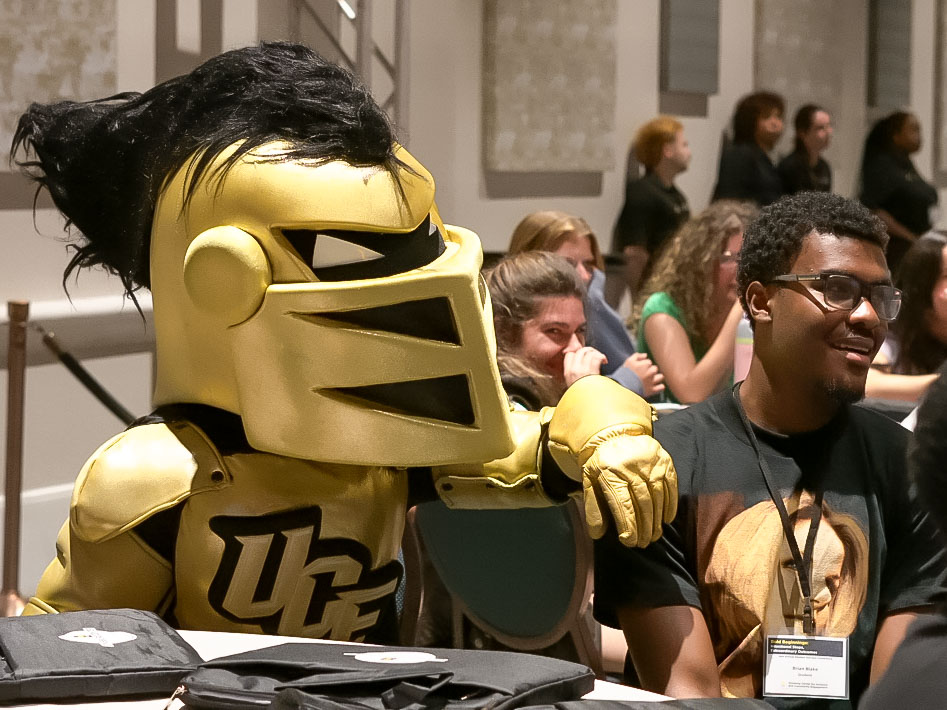 Knightro poses beside a student at a conference.
