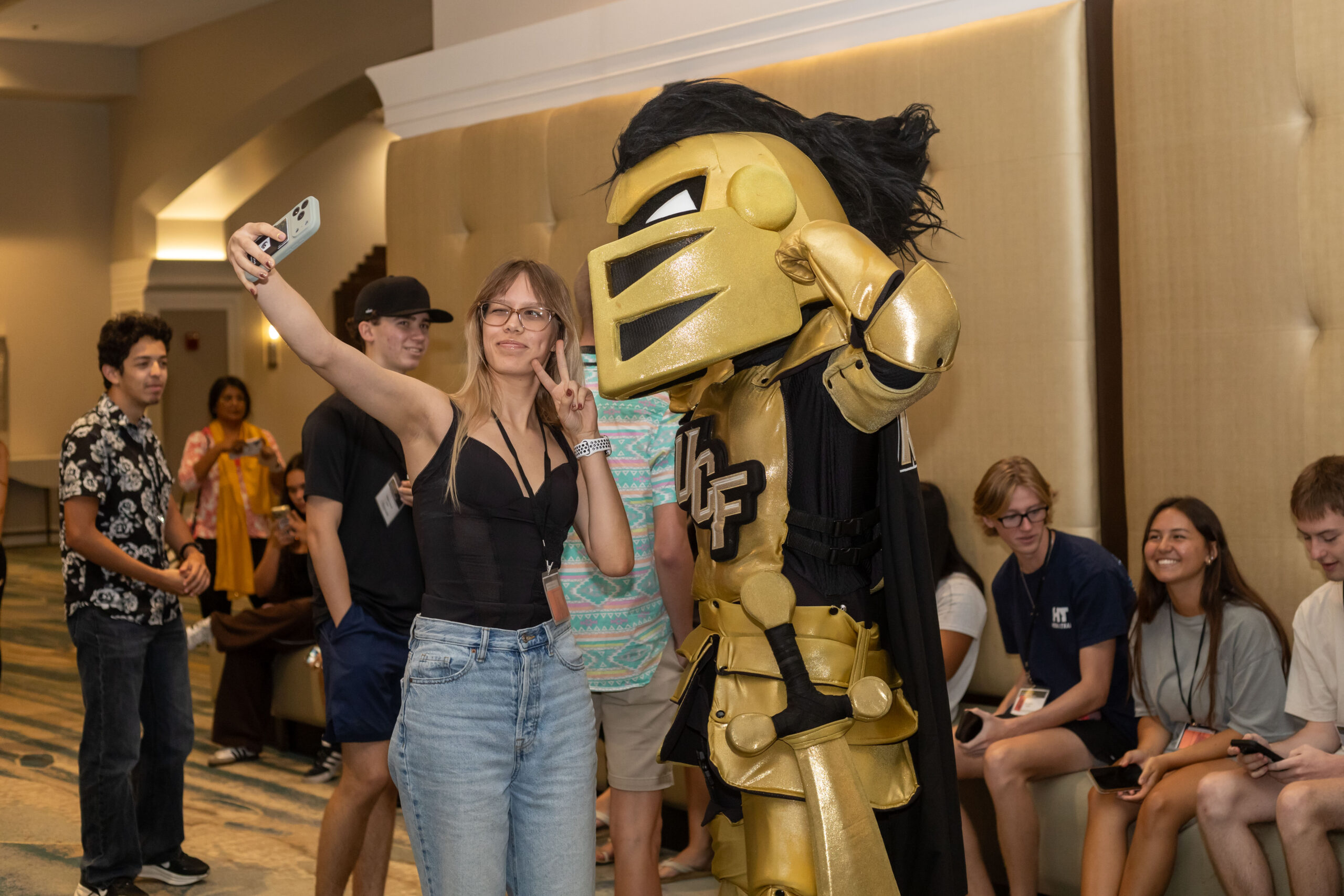 Attendees pose for a selfie with Knightro in gold-and-black armor at an indoor event.