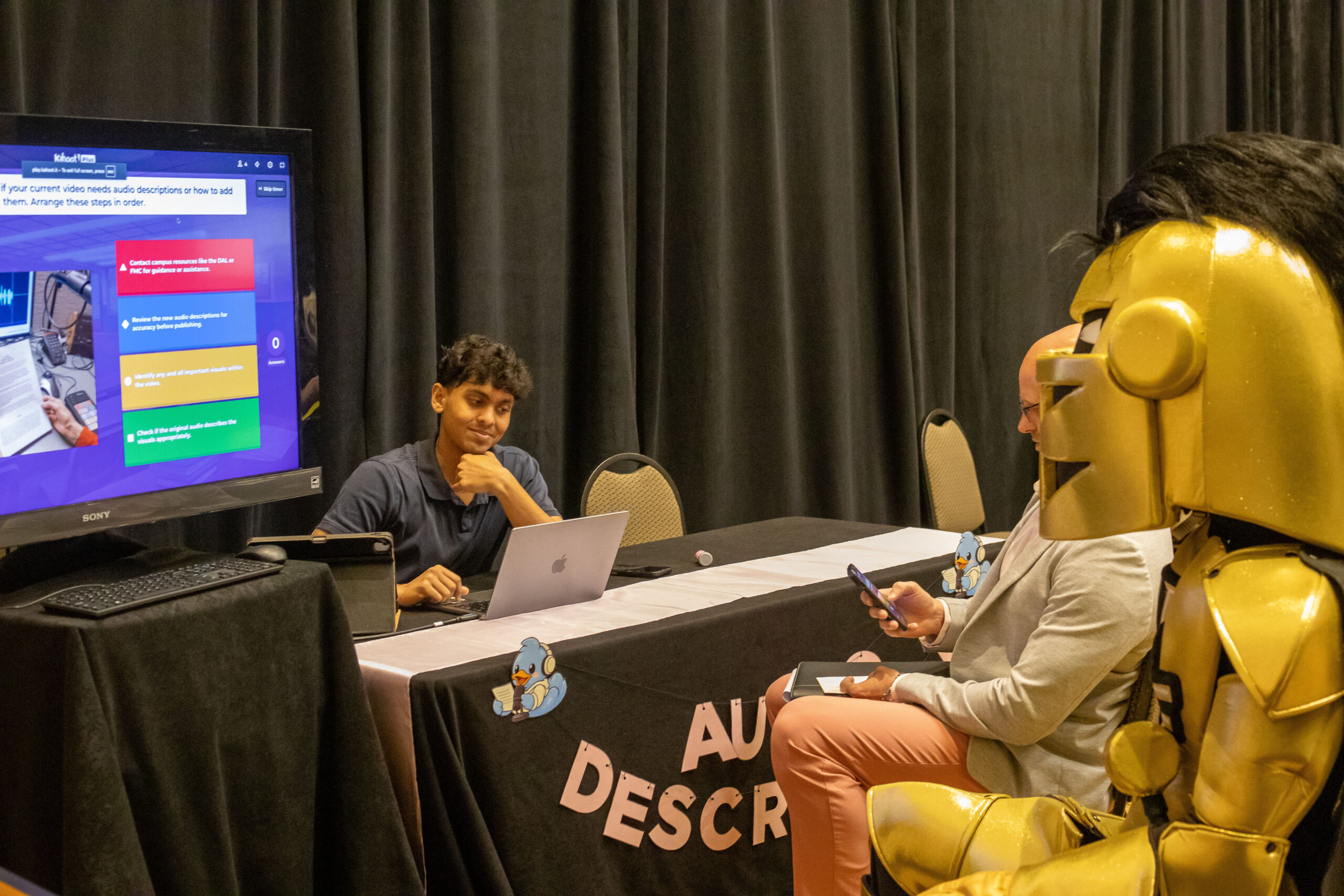 Attendees including Knightro particpating in a Kahoot game led by the Audio Description station facilitator