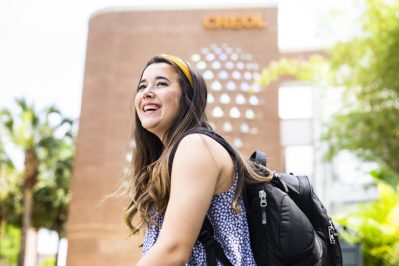 A female student with a backpack smiling while walking
