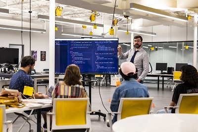 A professor teaching to a class with code on a monitor