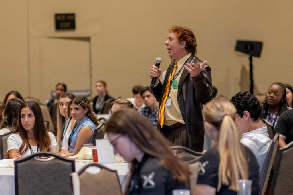 A student standing with a mic asking a question surrounded by others